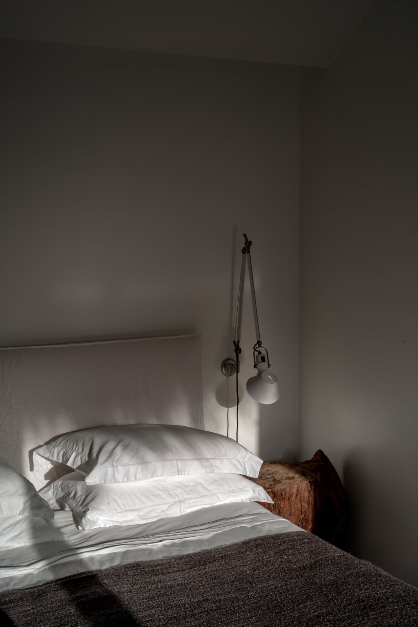 Casas na Areia, Europe — Minimalist bedroom with white linens, wooden headboard, pendant lamps on adjustable cords, and soft natural light casting shadows on white walls.