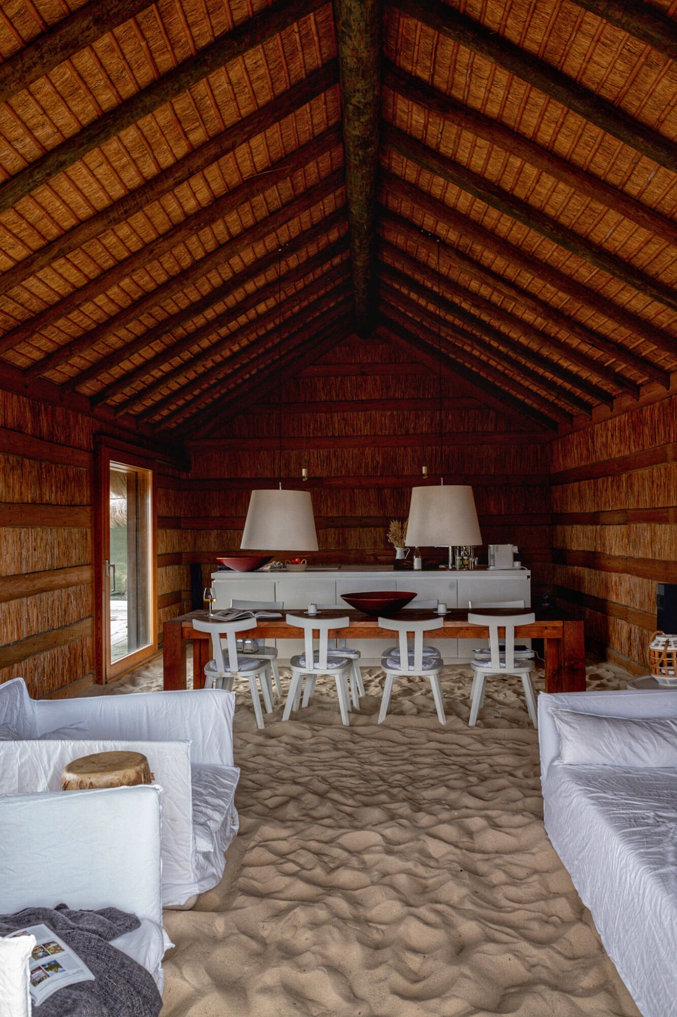 Casas na Areia, Europe — Timber beach pavilion with vaulted ceiling, sand floor, white furniture and wooden structural beams, minimalist coastal architecture.