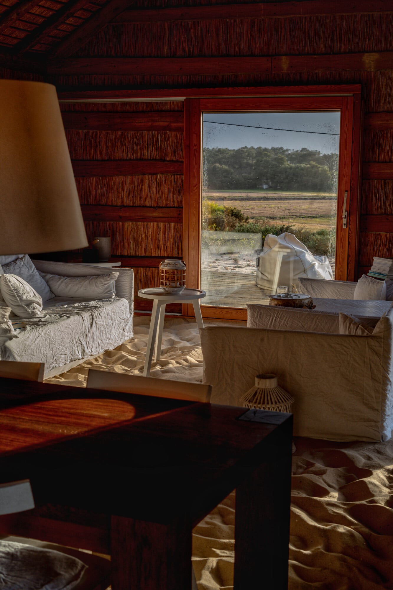 Casas na Areia, Europe — Wooden-beamed bedroom with linen furnishings, red-framed glass doors opening to marshland views, warm afternoon light.
