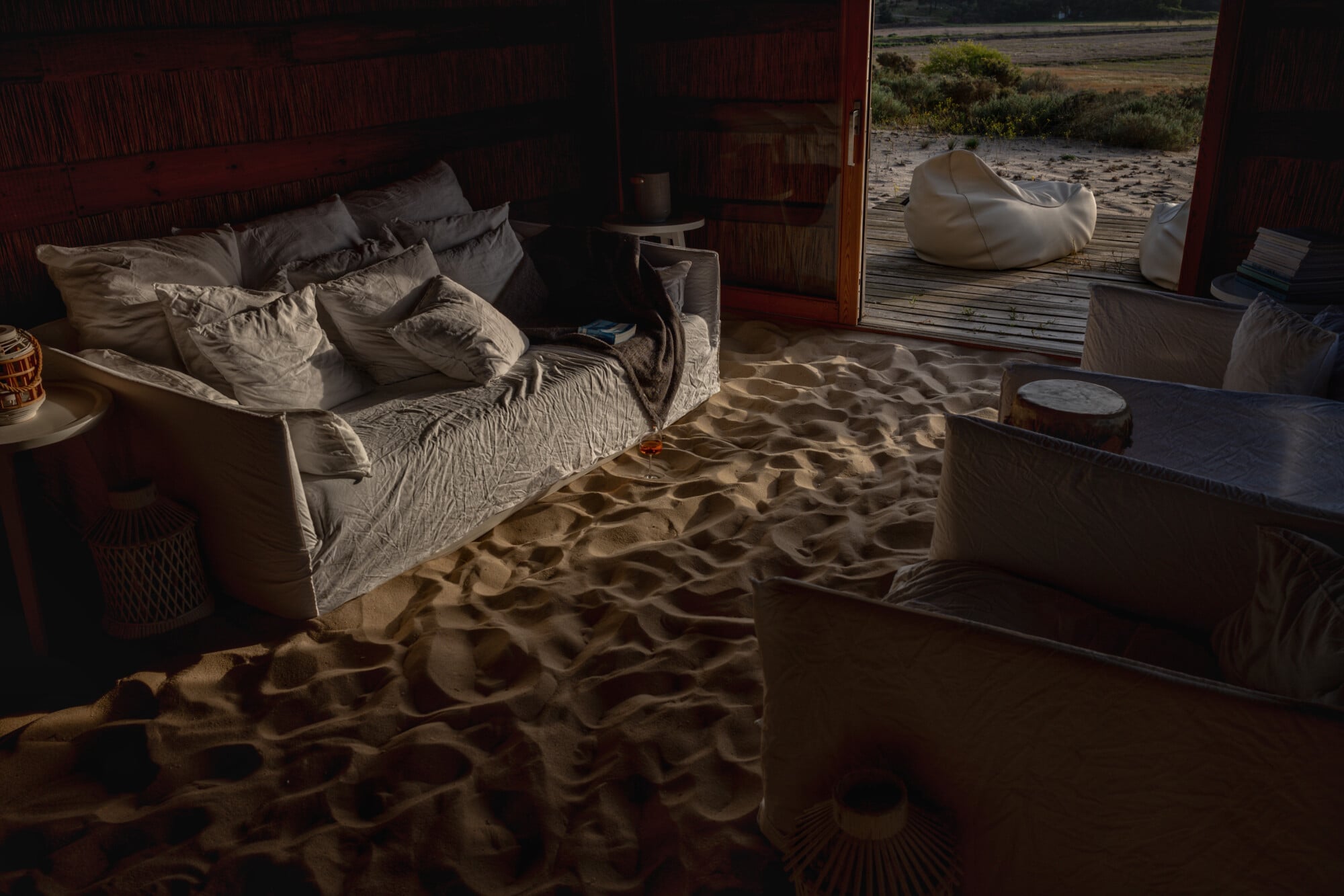 A beachfront bedroom at Casas na Areia with sand flooring, linen bedding, and ocean views through open doors.