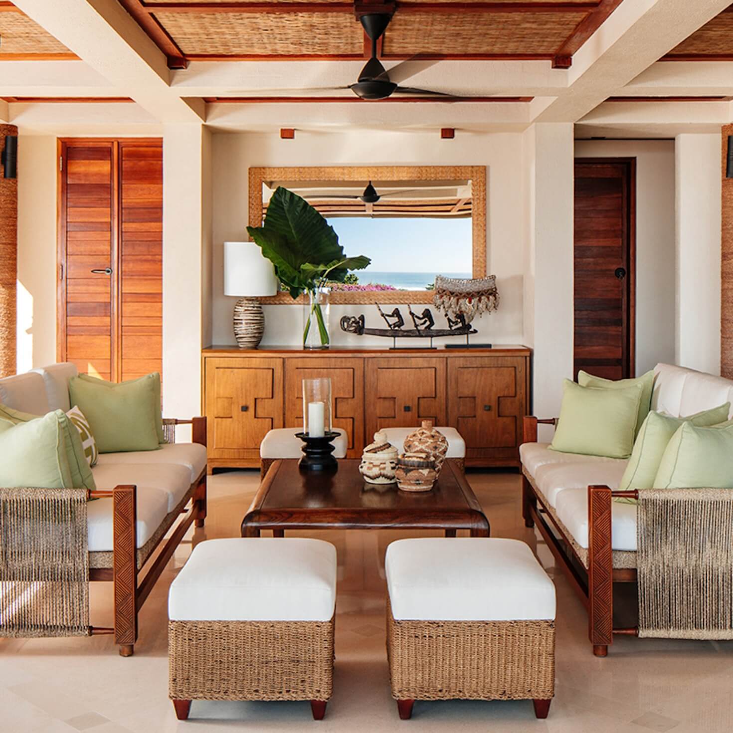 NIHI Sumba, Asia — Coastal living room with teak wood furnishings, woven ottomans, lime-green accents, ocean views, and coffered ceiling with natural light.