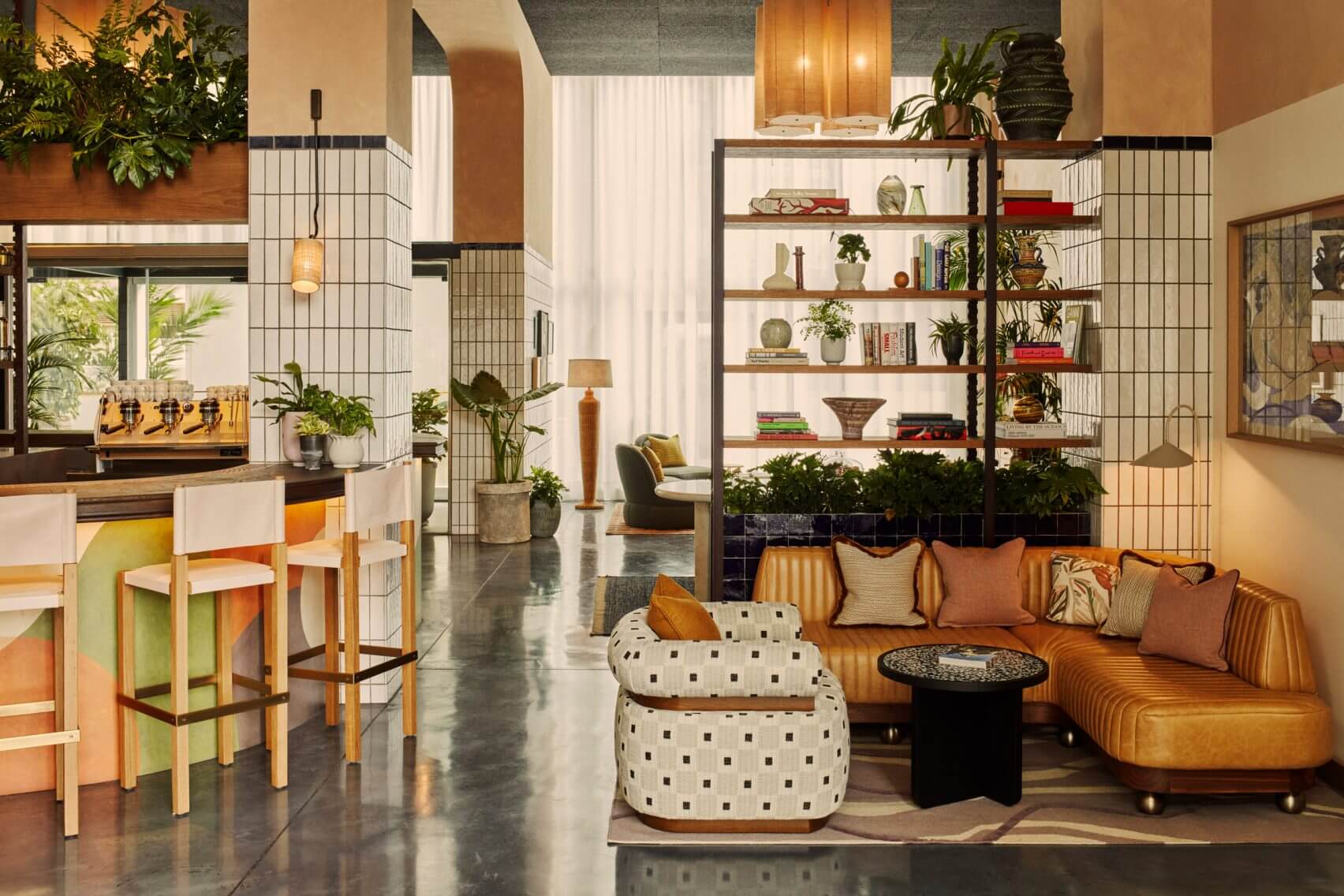 The Hoxton Poblenou, Barcelona, Spain — Open-plan living space with cognac leather sofa, brass shelving, potted plants, terrazzo accents, and black tile details.