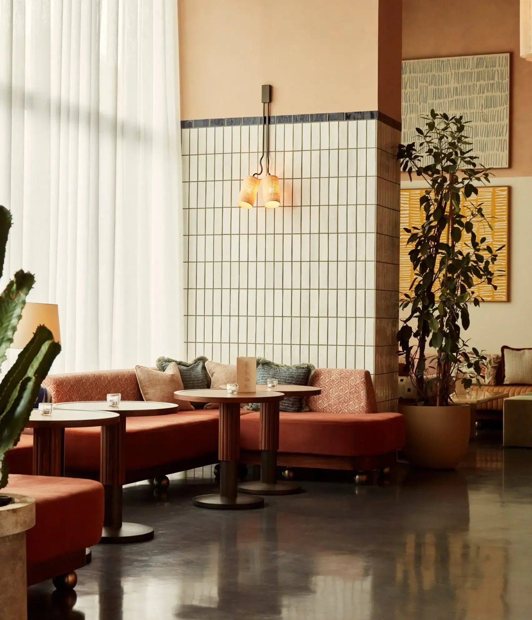 The Hoxton Poblenou, Barcelona, Spain — Terracotta lounge seating with wooden tables and pendant lighting beside gridded wall panel and tall potted plants.