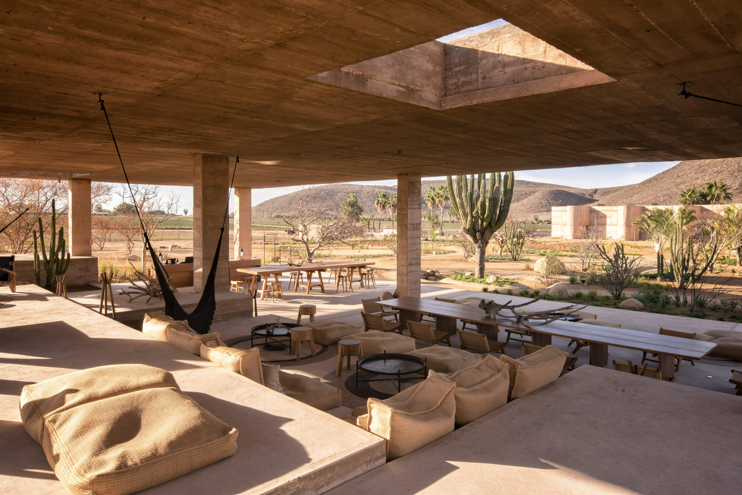 Paradero Todos Santos, Mexico — Open-air pavilion with concrete structure, woven seating, fire pits, and desert landscape views at sunset.