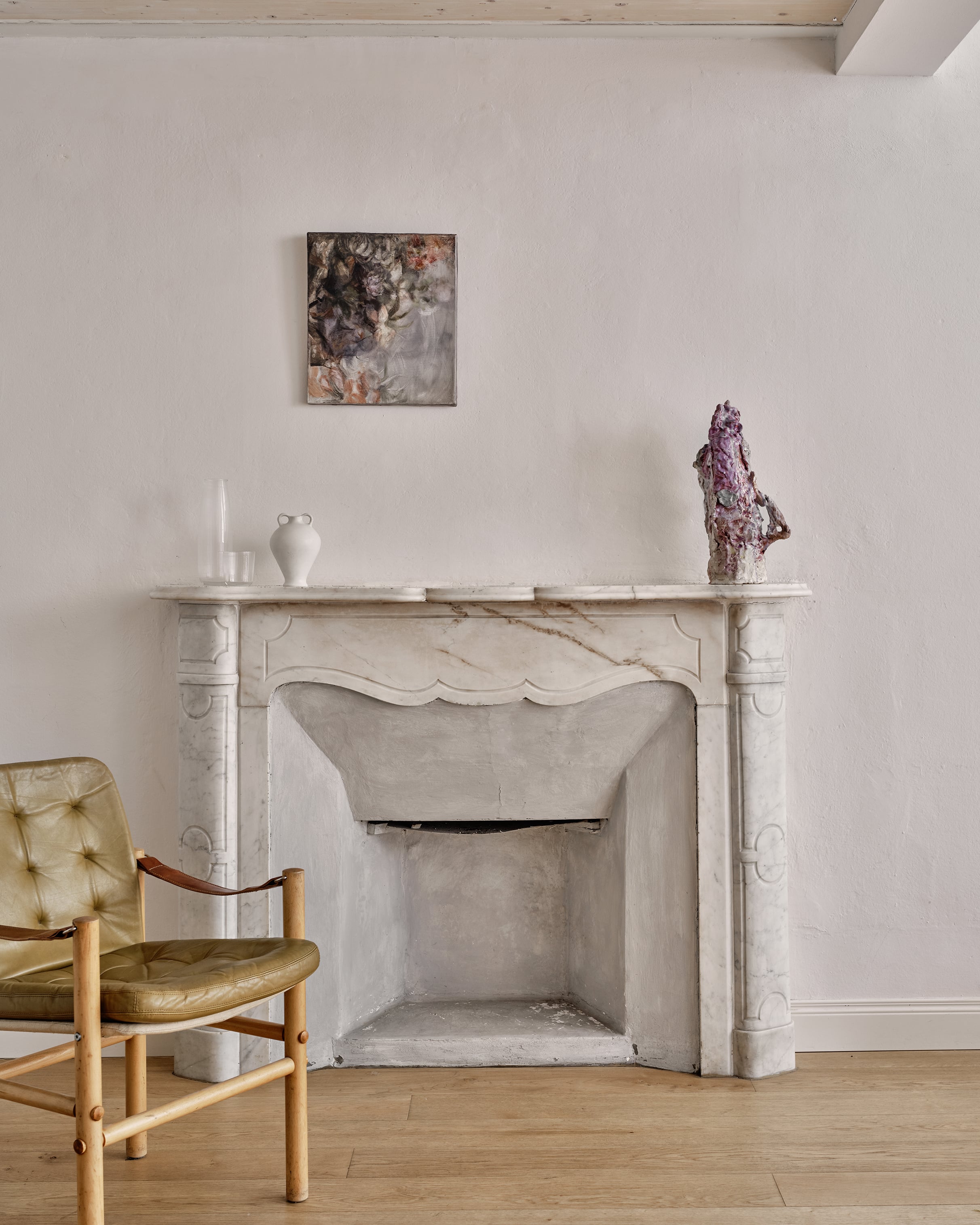 Numeroventi, Europe — Minimalist fireplace with marble surround, brass mid-century chair, curated objects, and framed artwork in serene neutral interior.