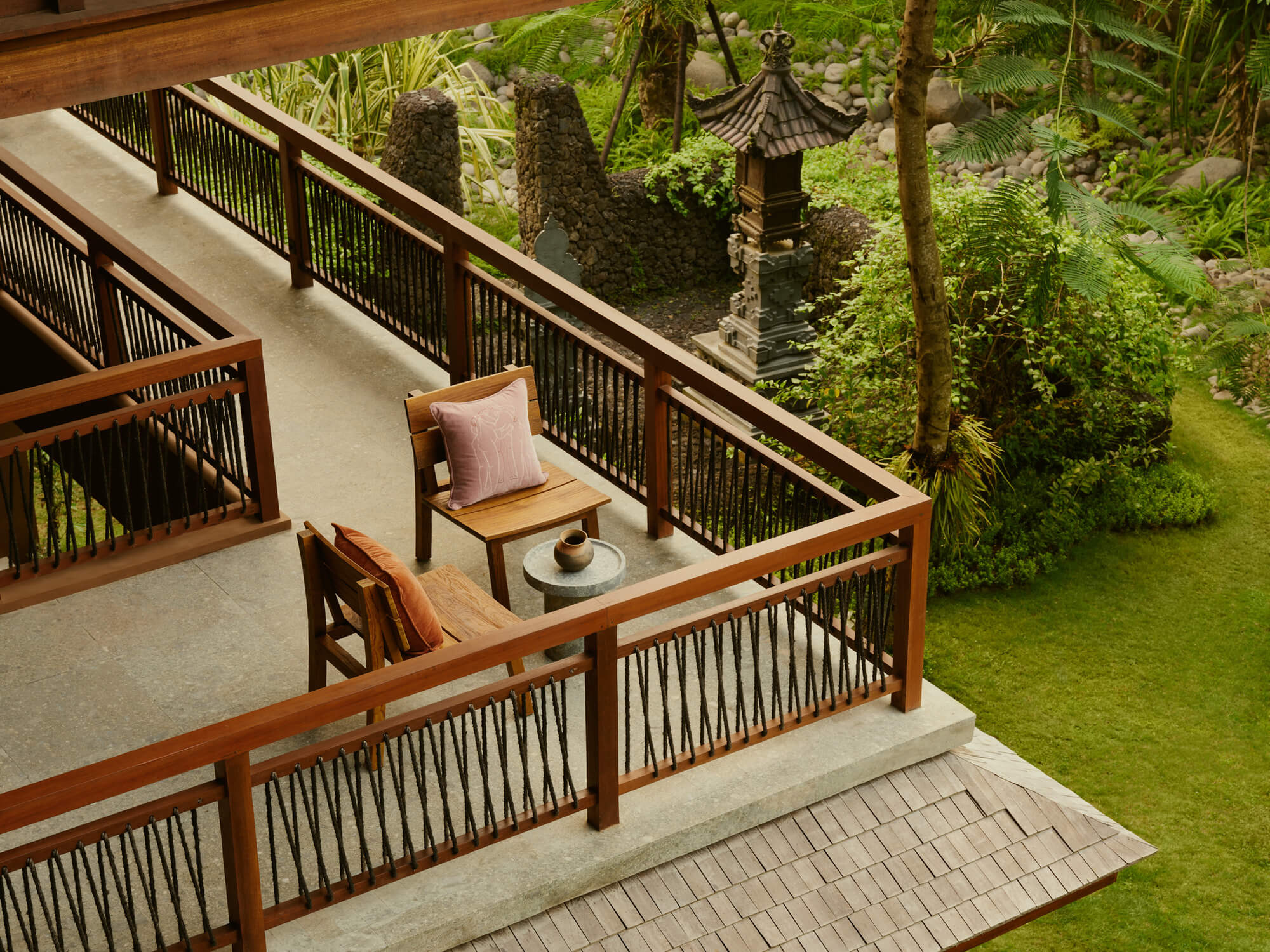 Lost Lindenberg, Asia — Wood-railed terrace overlooks lush garden with stone lantern, teak furniture, and layered tropical landscape bathed in natural light.