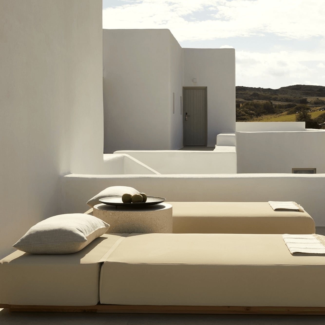 Pārocks, Europe — Minimalist white courtyard with geometric architecture, natural light, neutral textiles, and landscape vista.