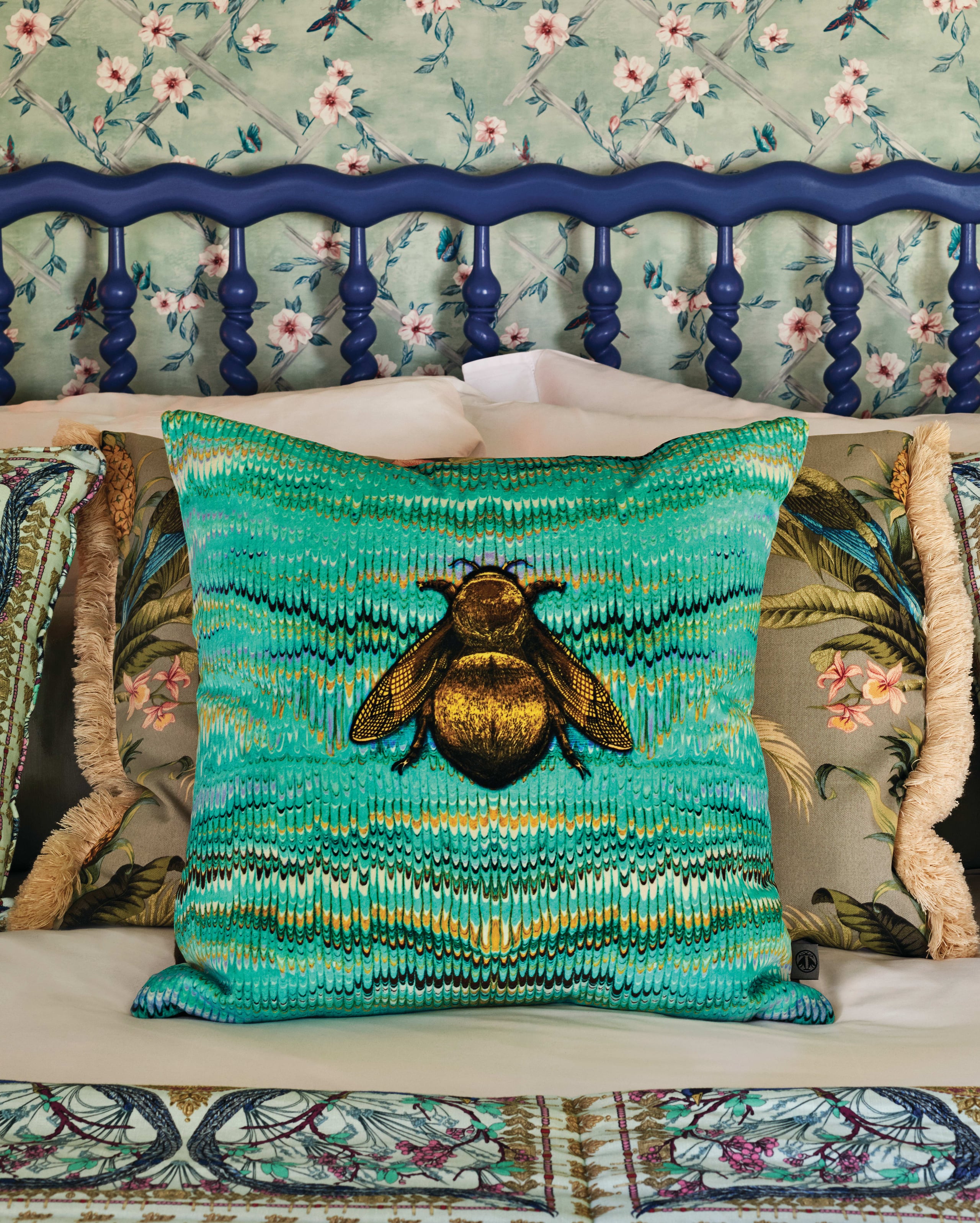 Belmond La Residencia, Balearic Islands — Turquoise embroidered bee cushion on floral headboard bed with navy spindle frame and botanical pillows.