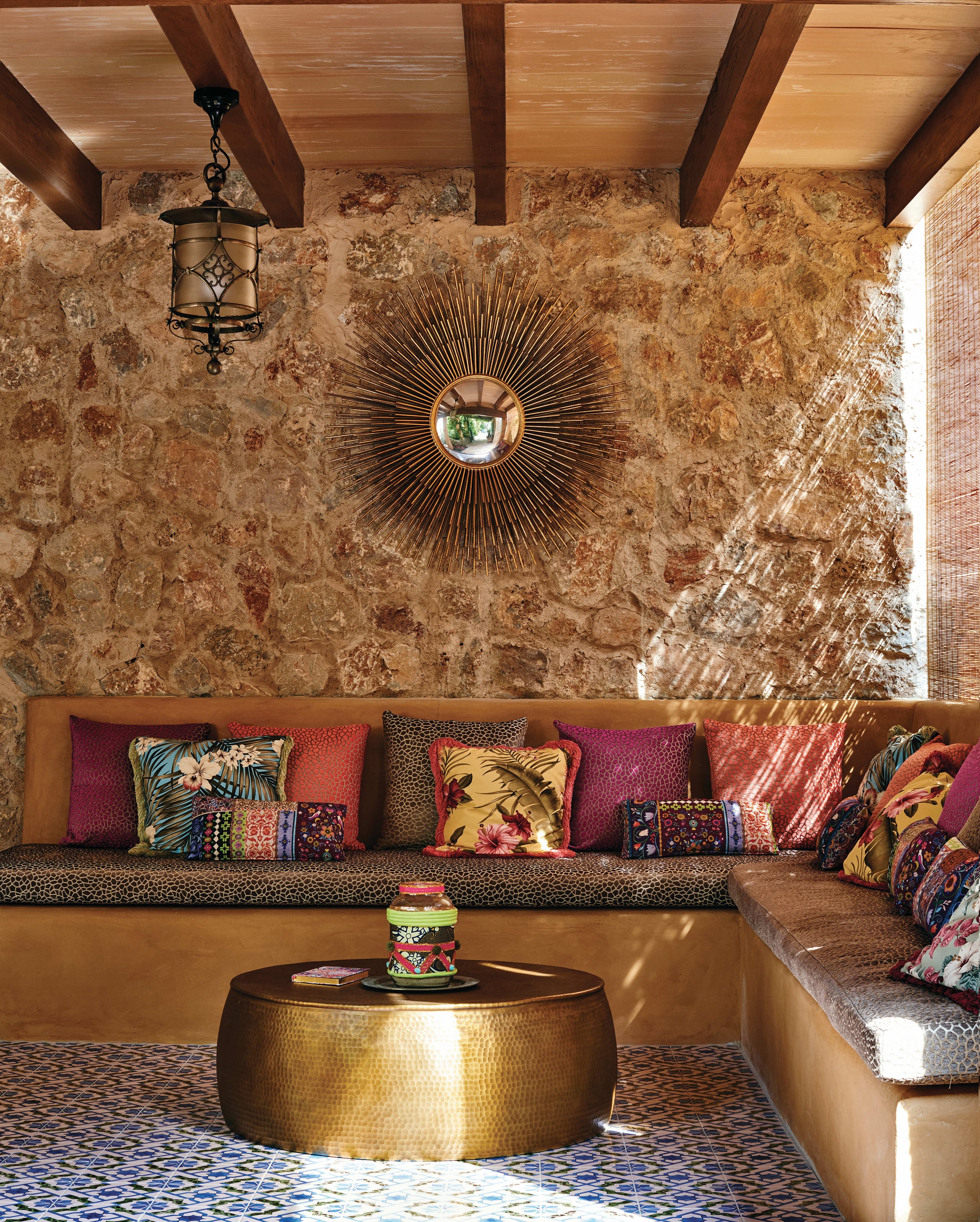 Belmond La Residencia, Balearic Islands, Spain — Stone courtyard with wooden beams, sunburst mirror, brass table, colorful pillows on built-in seating, Moorish tiles.