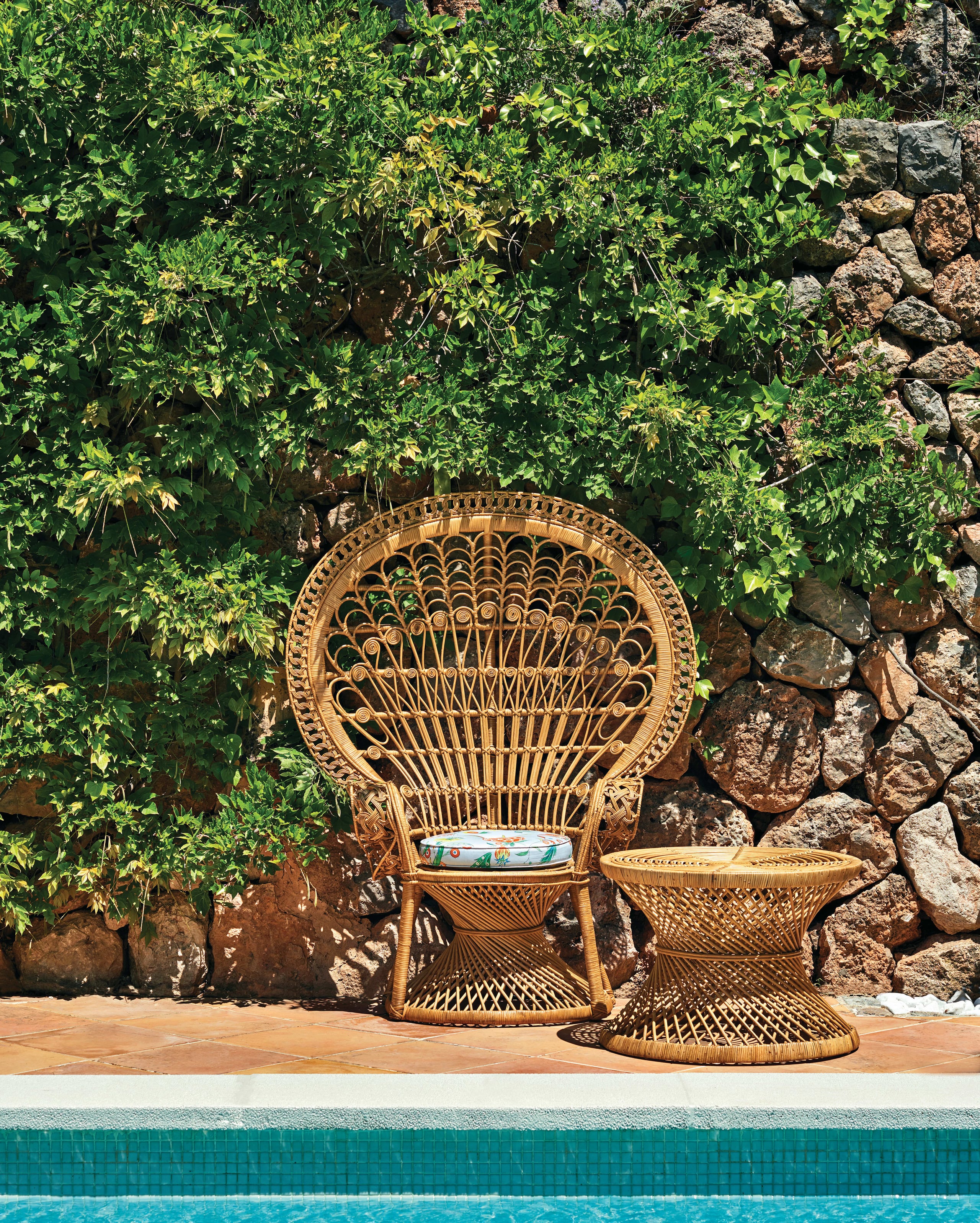 Belmond La Residencia, Balearic Islands — Woven rattan peacock chair beside stone wall and ivy-draped courtyard overlooking turquoise pool.