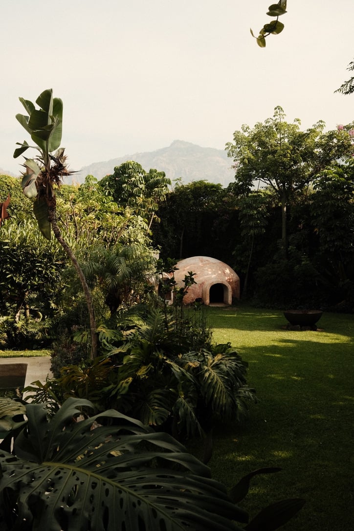 Casa Lumeria, Mexico — Terracotta dome structure nestled in lush tropical garden with mountain vista, contemporary architecture blending earthy materials and verdant landscape.