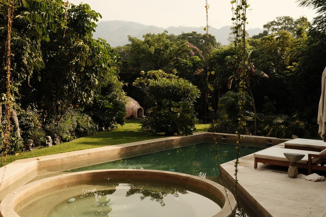 Casa Lumeria, Mexico — Curved stone pools with lush jungle garden, mountains, and afternoon light filtering through tropical vegetation.