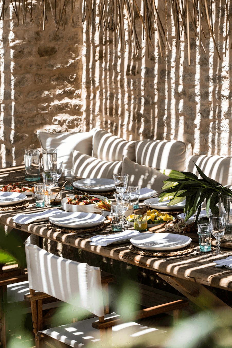 Arijiju Retreat, Africa — Outdoor dining setup with striped cushions, wooden table, white place settings, and birch forest backdrop in dappled sunlight.
