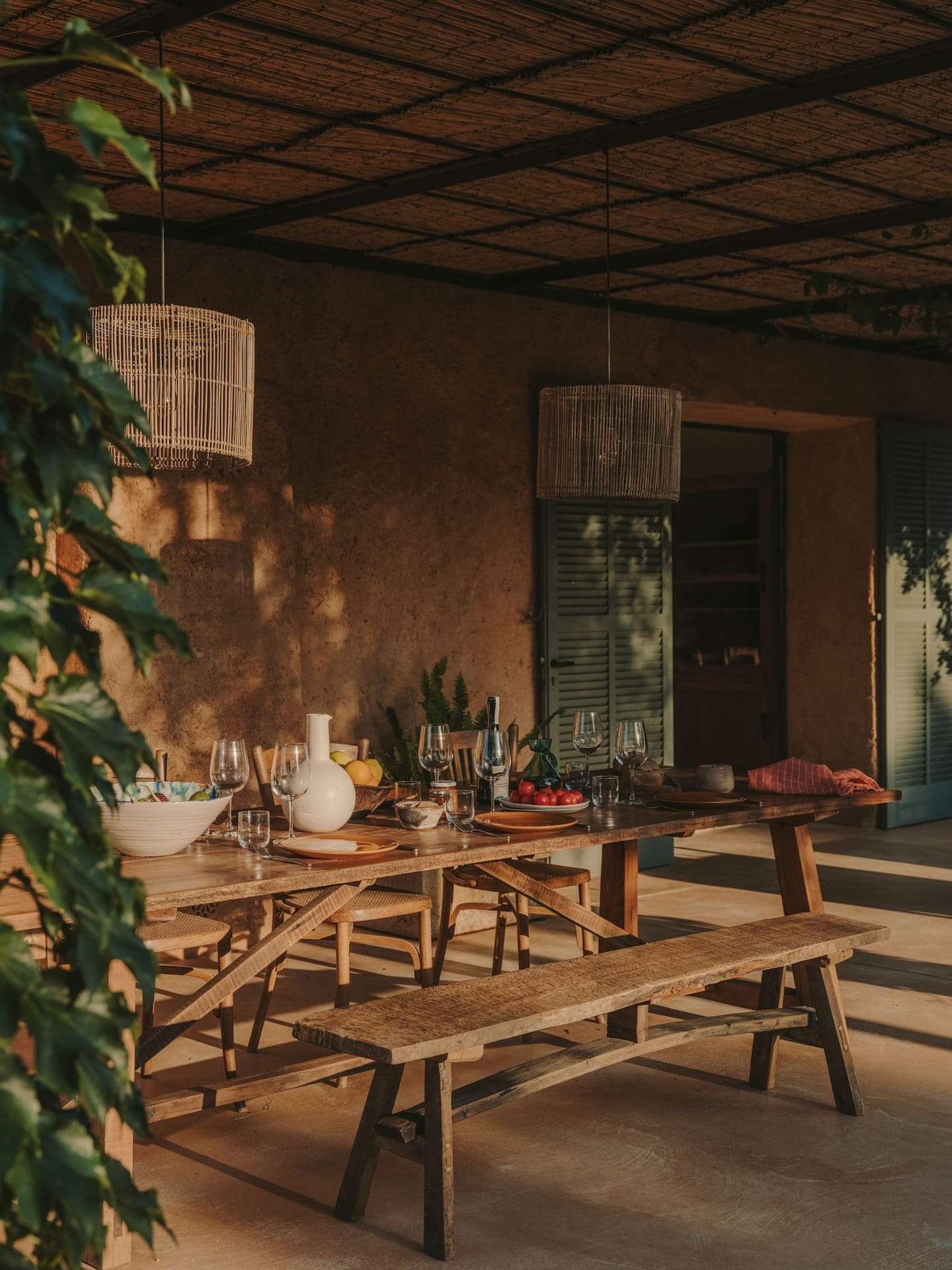 Can Lluïssó, Balearic Islands, Spain — Ochre terracotta courtyard with wooden dining table, woven pendant lights, and vine-covered walls at sunset.