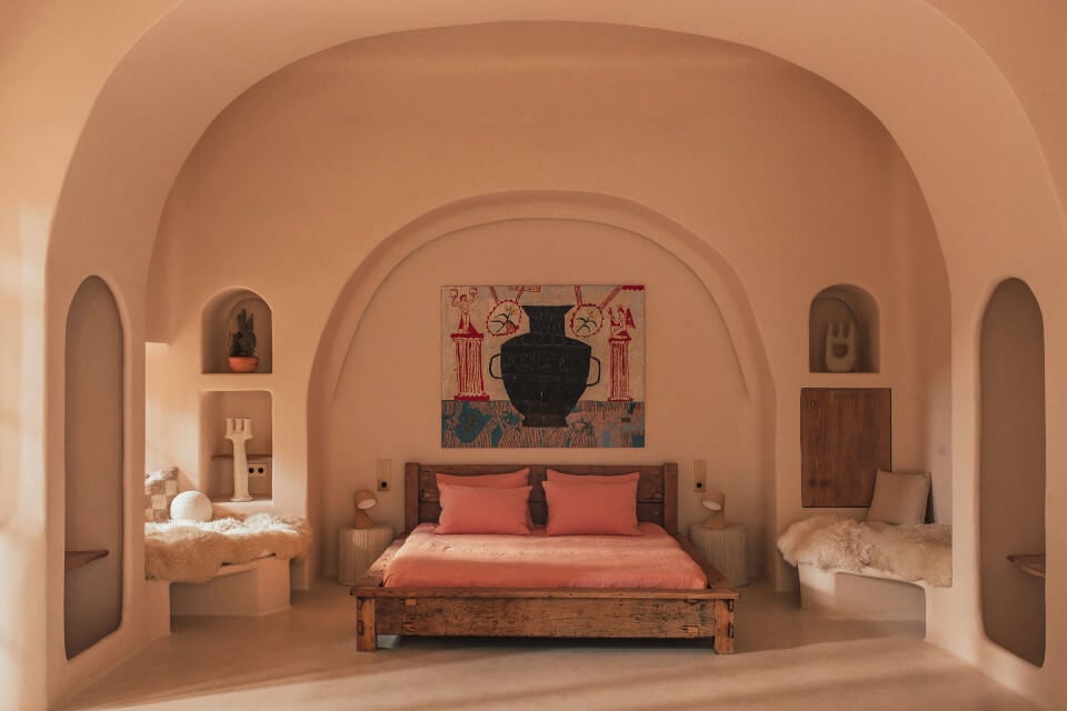 Hotel Corazón, Balearic Islands — Terracotta arched bedroom with coral bedding, wooden bed frame, sculptural niches, and ochre-toned minimalist design.