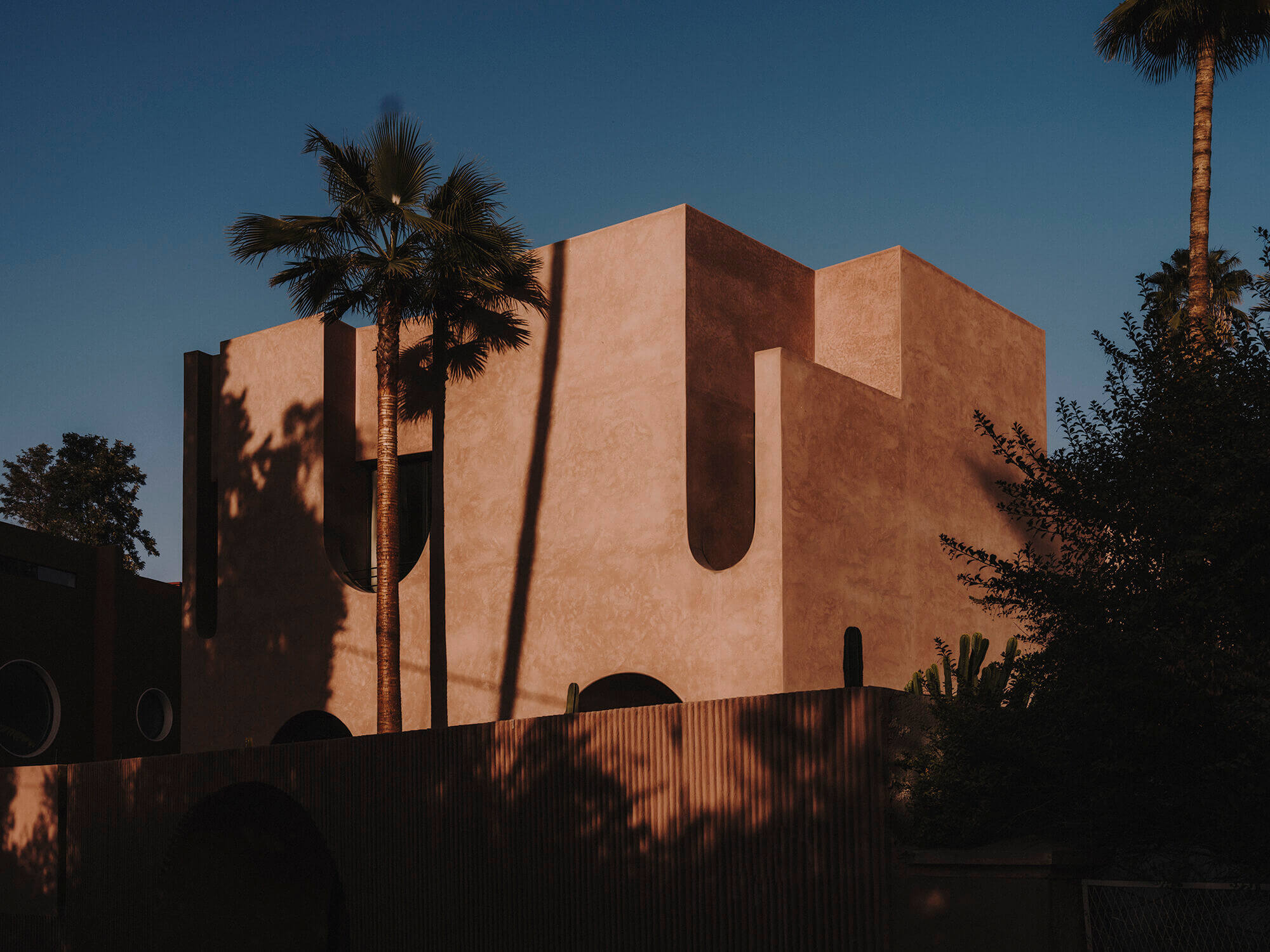 Maison Brummell Majorelle, Africa — Terracotta modernist villa with curved apertures and geometric forms, palm tree shadows cast across ochre facade at golden hour.