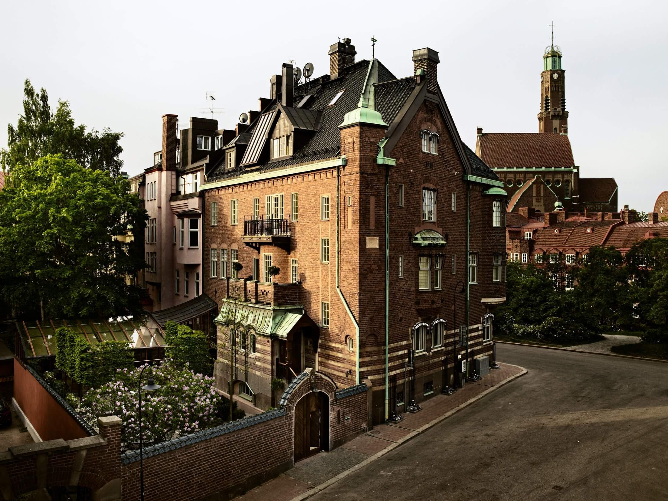 Ett Hem, Europe — Red brick Scandinavian villa with green copper roof, ornate chimneys, and manicured gardens in afternoon light.