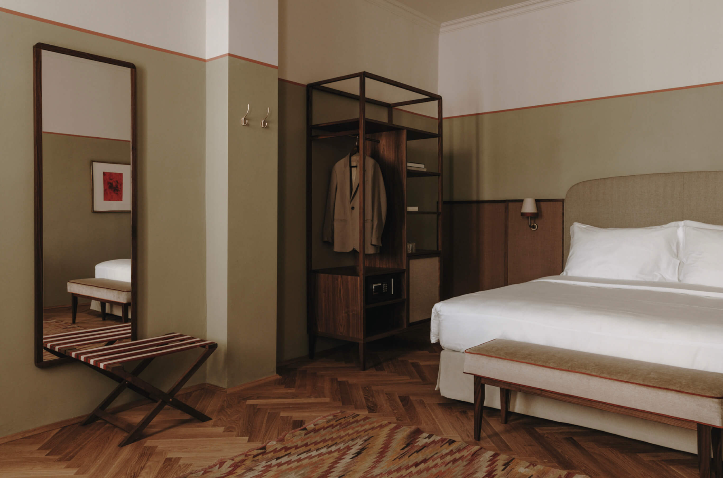 Parkhotel Mondschein, Europe — Mid-century modern hotel bedroom with dual beds, walnut wood wardrobe, herringbone flooring, sage walls with coral accent stripe, and full-length mirror.