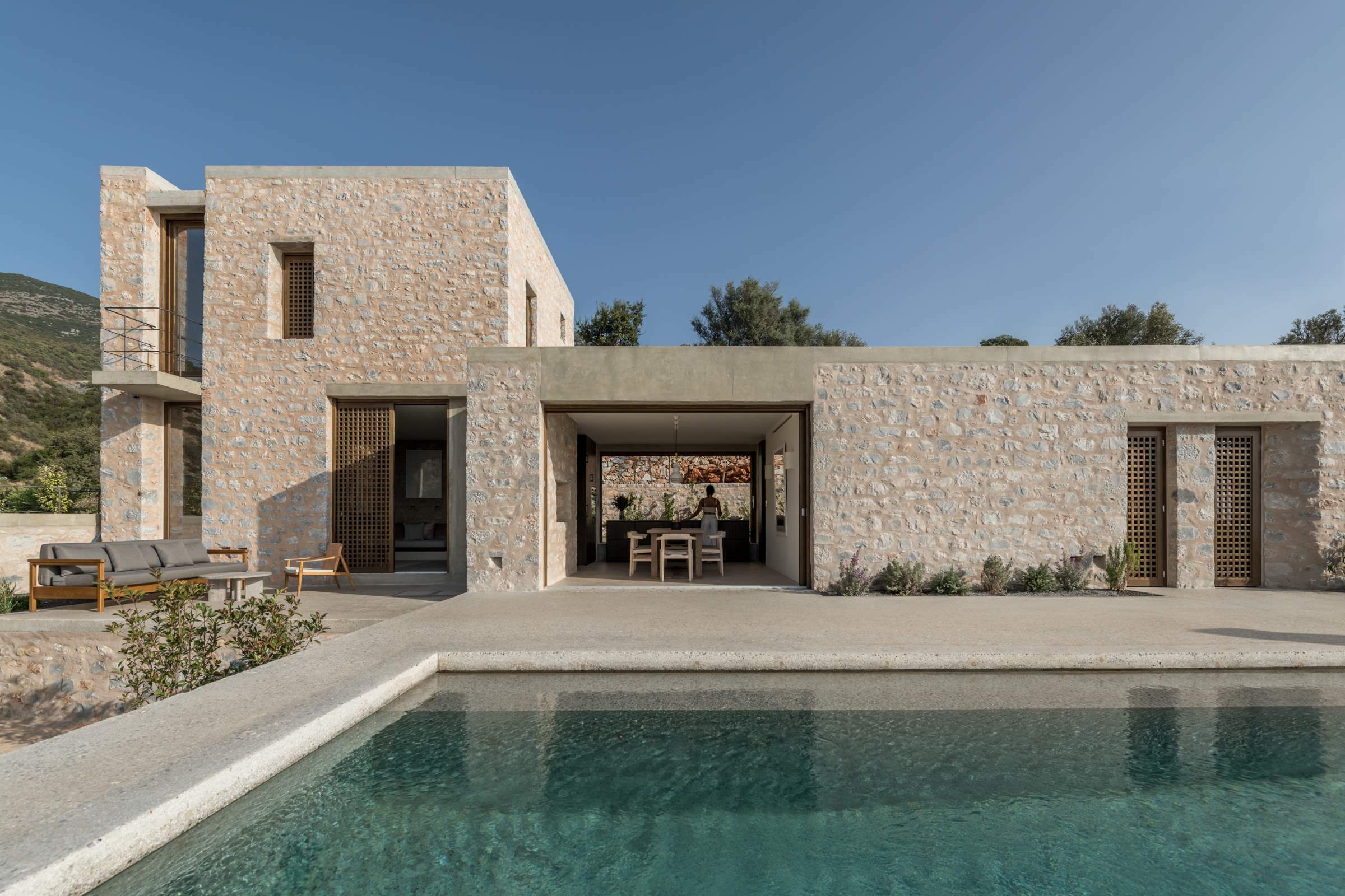 Monolithoi, Europe — Stone villa with pool, minimalist architecture, warm limestone facade, geometric forms, Mediterranean landscape, luxury resort design.