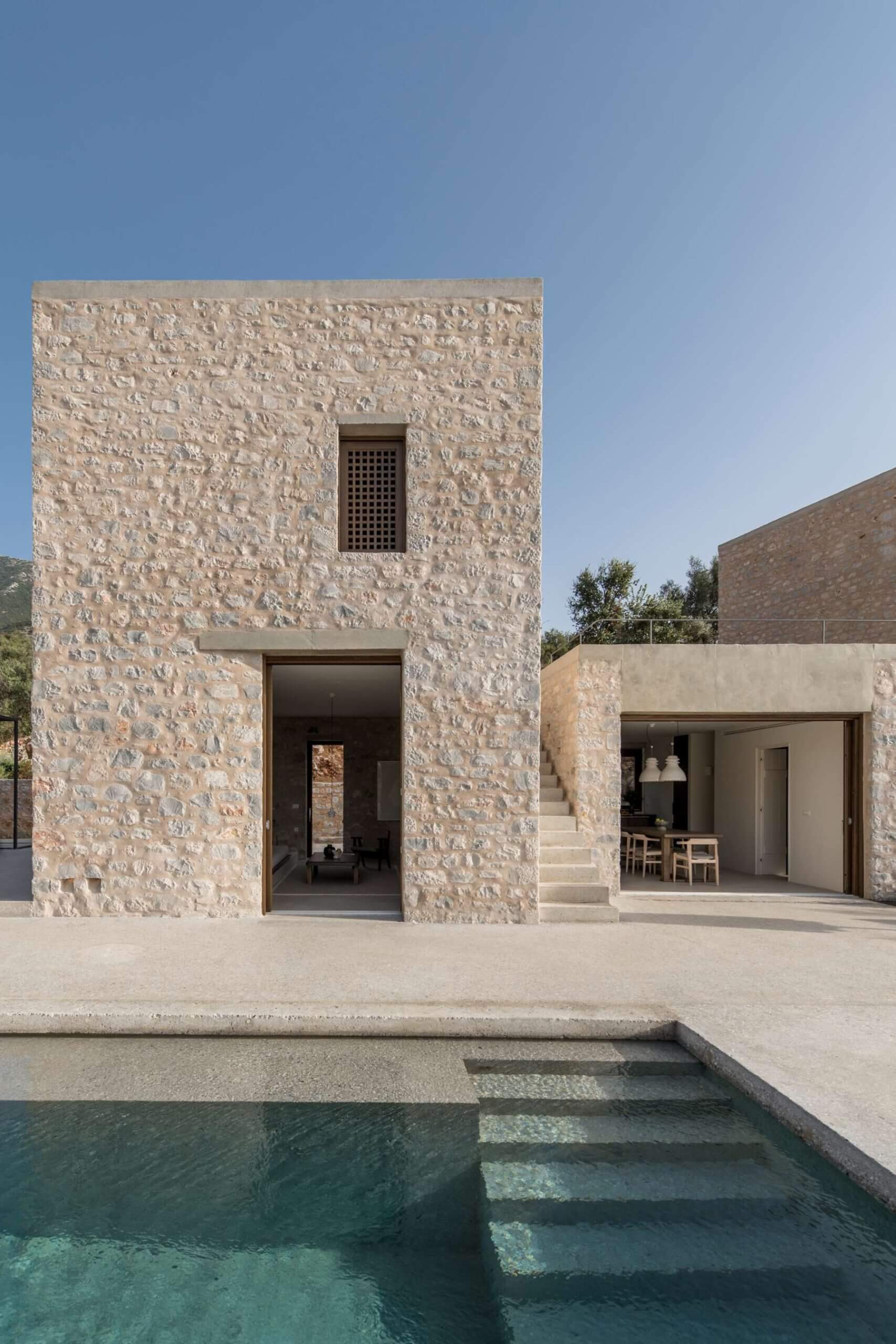 Monolithoi, Europe — Minimalist stone villa with geometric facade, stepped pool, and open-air courtyard overlooking Mediterranean landscape.