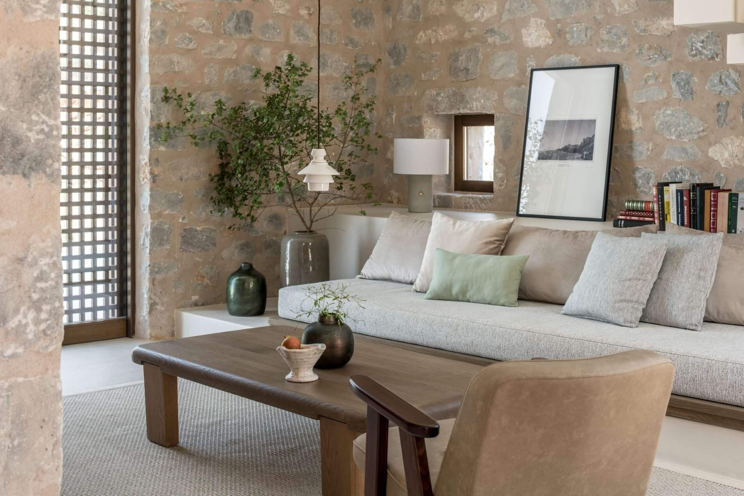 Monolithoi, Europe — Minimalist living room with stone walls, linen sofa, wooden coffee table, and natural light from latticed window.