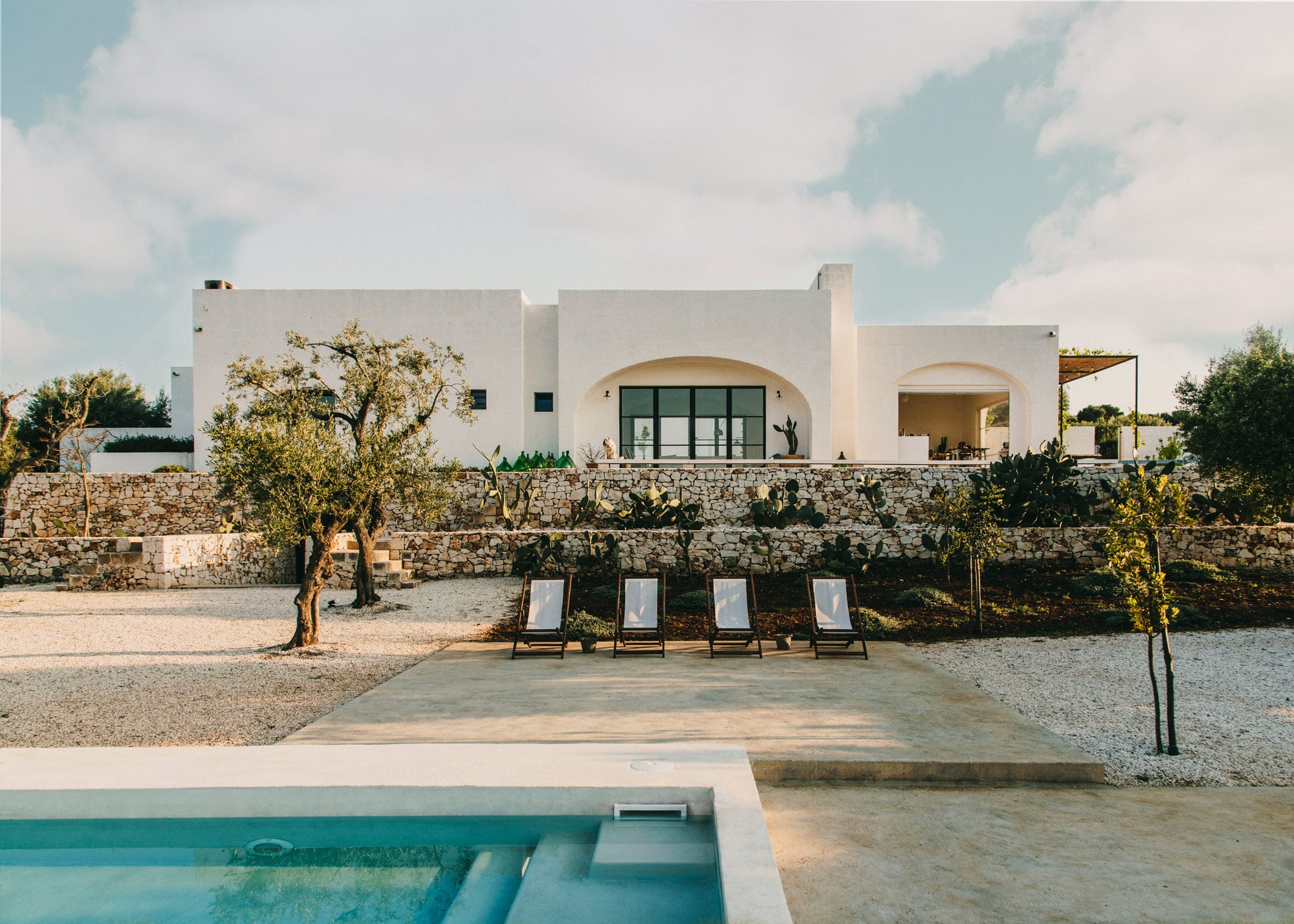 Moroseta Cooking Class, Europe — whitewashed modernist villa with curved archways, stone terrace, olive trees, and pool overlooking Mediterranean landscape at golden hour.