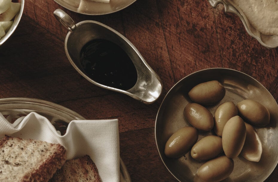 Luna Bar, Europe — Overhead view of bread, roasted potatoes, gravy boat, and place setting on warm wood table in intimate dining atmosphere.