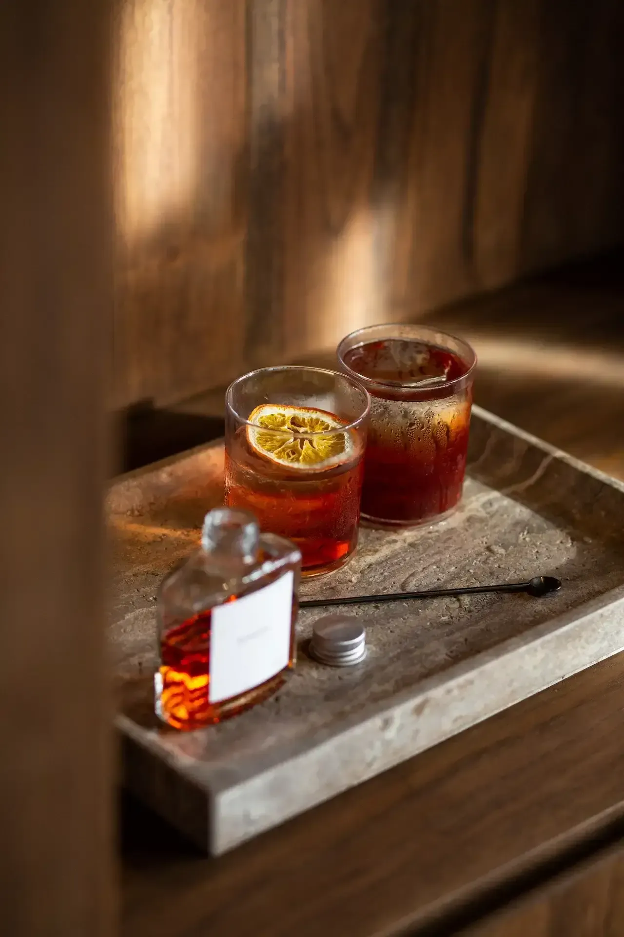 Further Hotel, Asia — Two amber cocktails with lemon garnish on concrete tray, warm window light, minimalist luxury bar styling.
