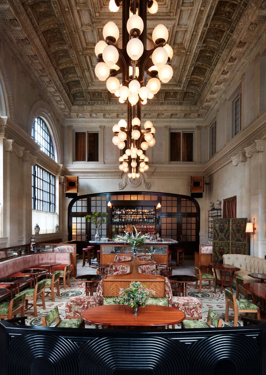 Nine Orchard, New York, USA — Coffered ceiling with ornamental plasterwork, brass globe chandelier, mid-century modern furniture, and bar lounge in historic beaux-arts lobby.