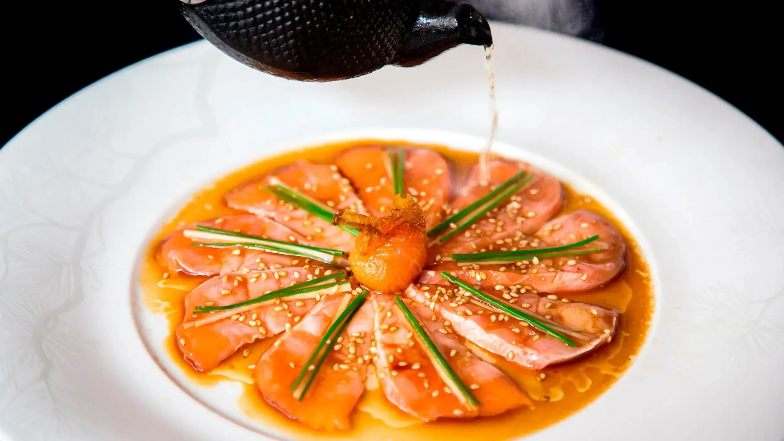 Nobu Restaurant, Mexico — Chef plating seared salmon carpaccio with sesame seeds, chives, and amber citrus sauce in fine dining presentation.