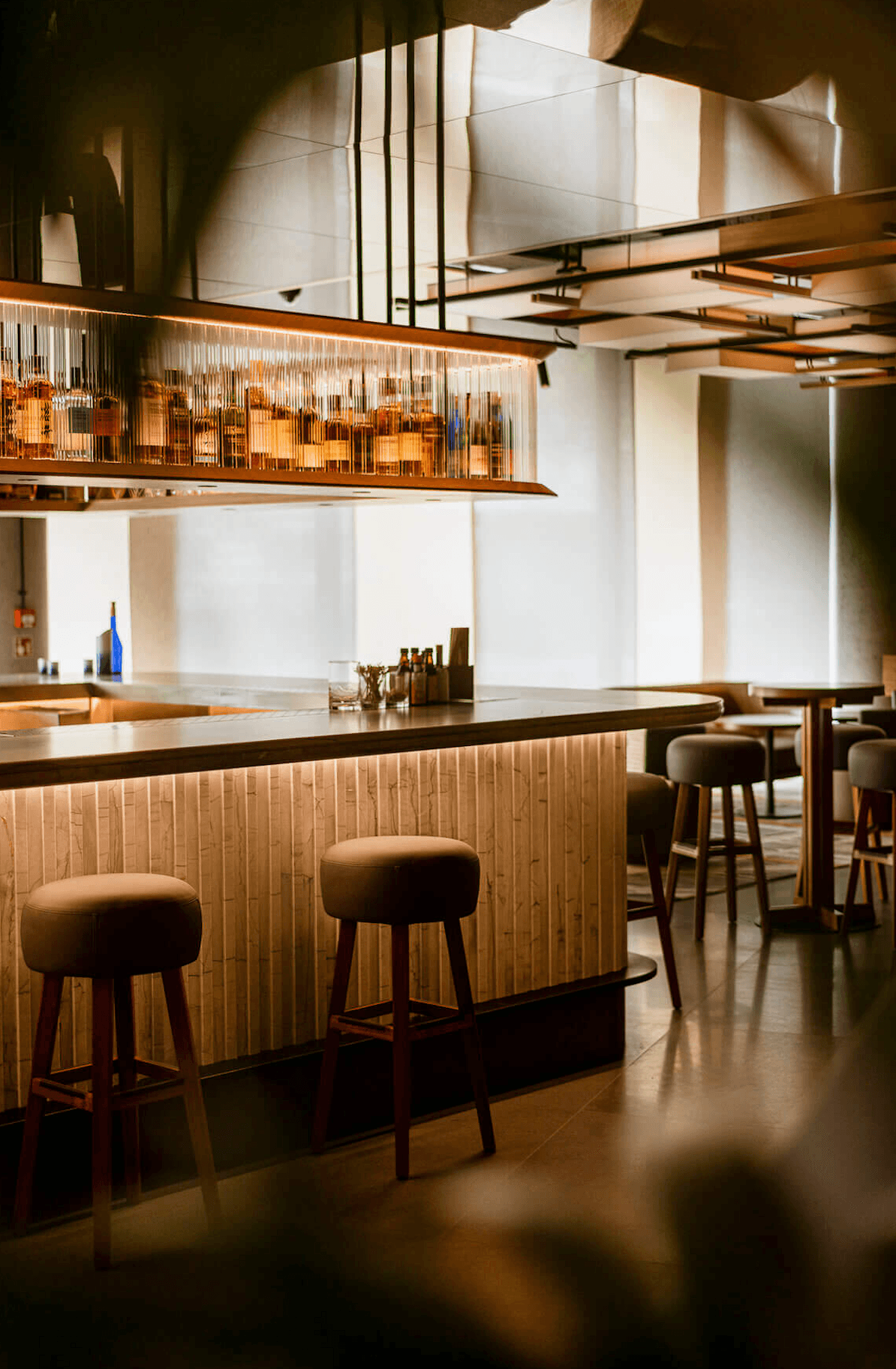 Nobu Warsaw, Poland — Modern bar interior with warm wood paneling, brass pendant lighting, and leather bar stools beneath sculptural cityscape installation.
