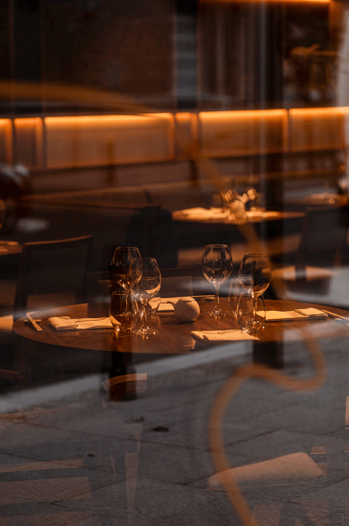 Nobu Warsaw, Poland — Candlelit round dining table with wine glasses and place settings at golden hour, minimalist luxury restaurant interior with floor-to-ceiling windows.