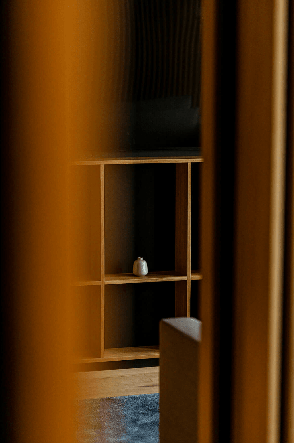 Nobu Warsaw, Poland — Minimalist wooden shelving unit with ceramic vessel, warm ambient lighting, and flowing curtains creating serene hospitality interior design.