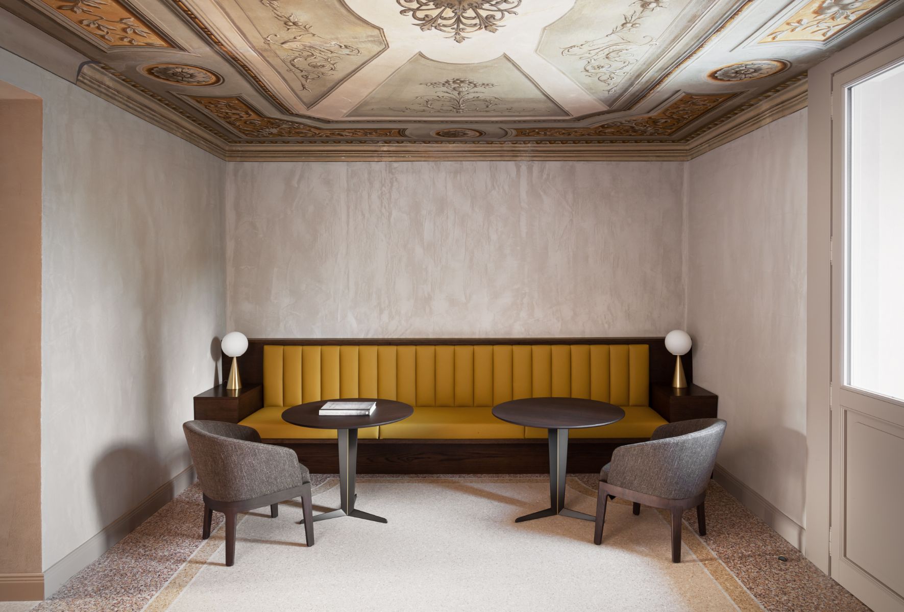 Roncolo 1888, Europe — Ochre velvet banquette with frescoed ceiling, paired marble tables, modernist chairs, and ornate plasterwork in luxury hospitality lounge.