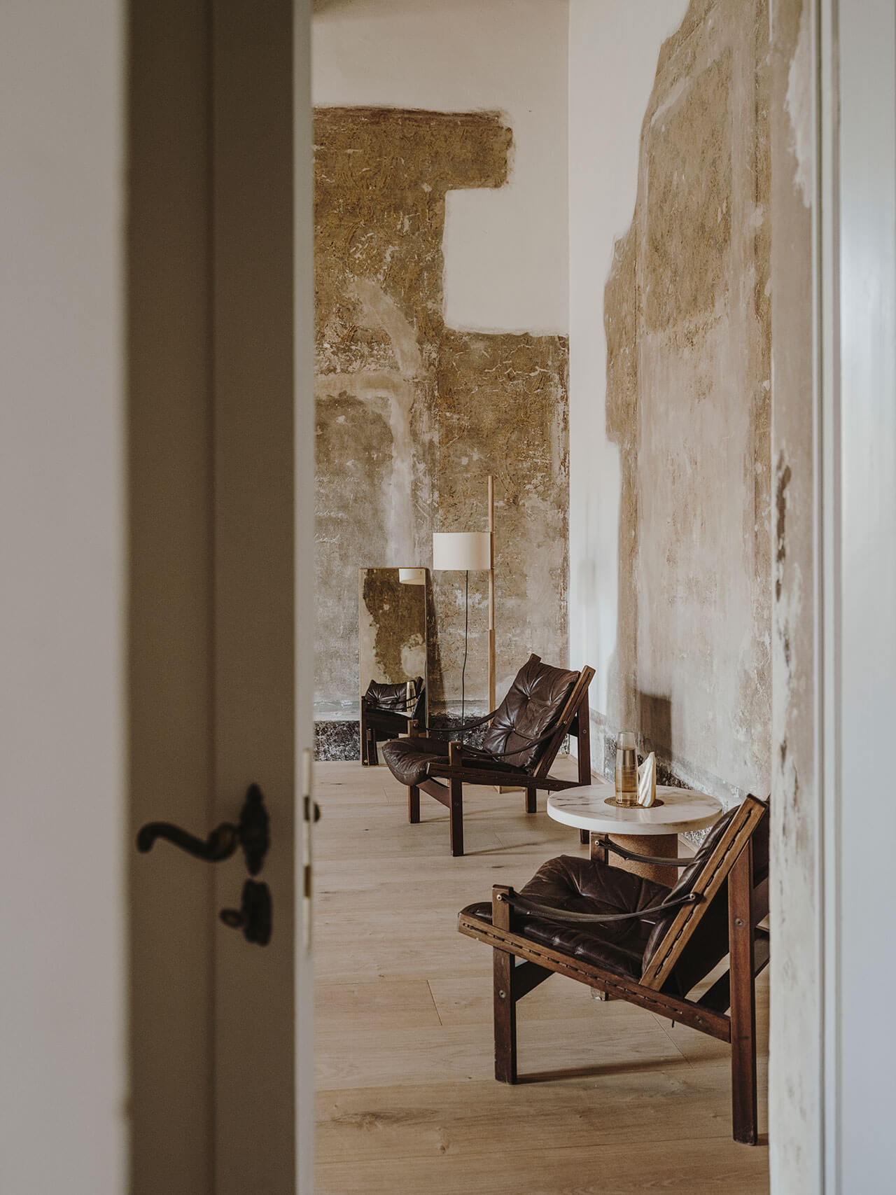 Numeroventi, Europe — Minimalist gallery space with distressed plaster walls, leather sling chairs, pale wood flooring, and curated furniture displaying refined industrial aesthetic.