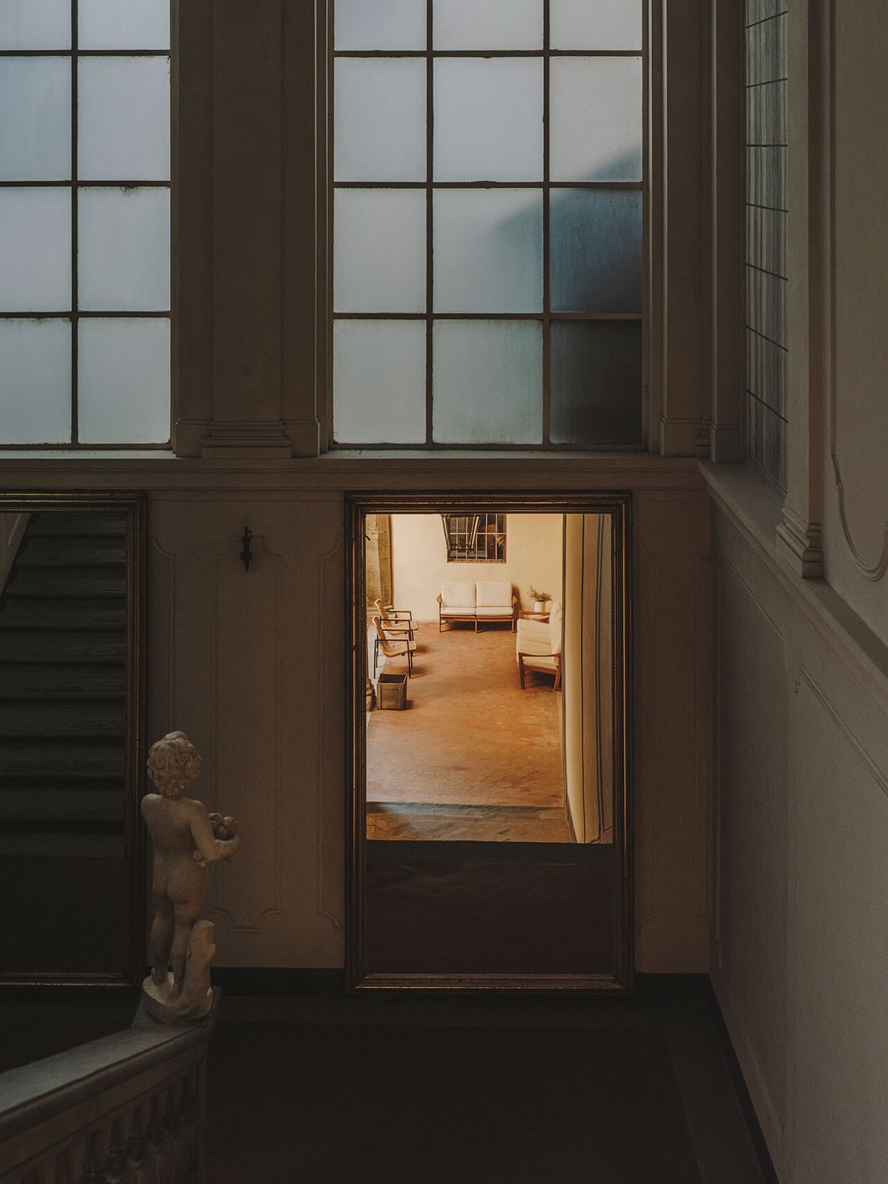 Numeroventi, Europe — Modernist corridor with glazed door opening to minimalist lounge, natural wood flooring, crisp daylight, sculptural detail.