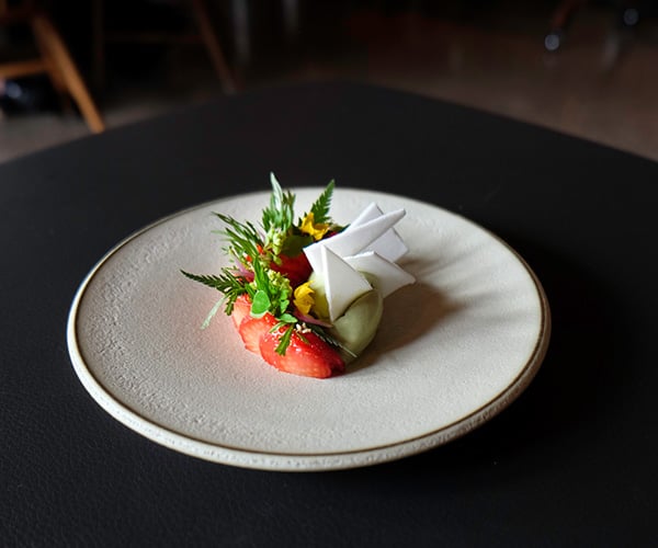 Oaxen Krog, Europe — Plated dessert with strawberry, white chocolate, fresh herbs, and edible flowers on minimalist ceramic dish, fine dining presentation.
