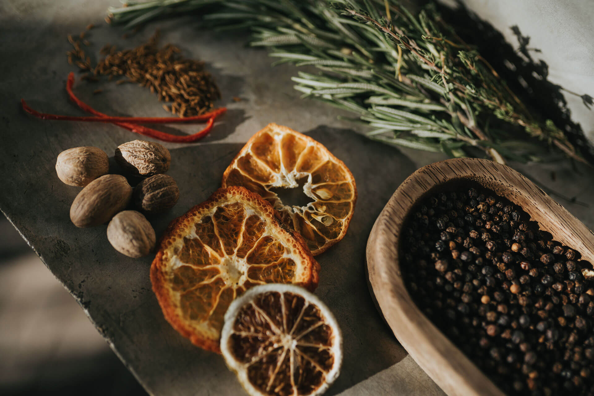 Be Tulum, Mexico — Dried citrus slices, nuts, and peppercorns arranged on concrete with fresh rosemary and red chili, natural light styling.