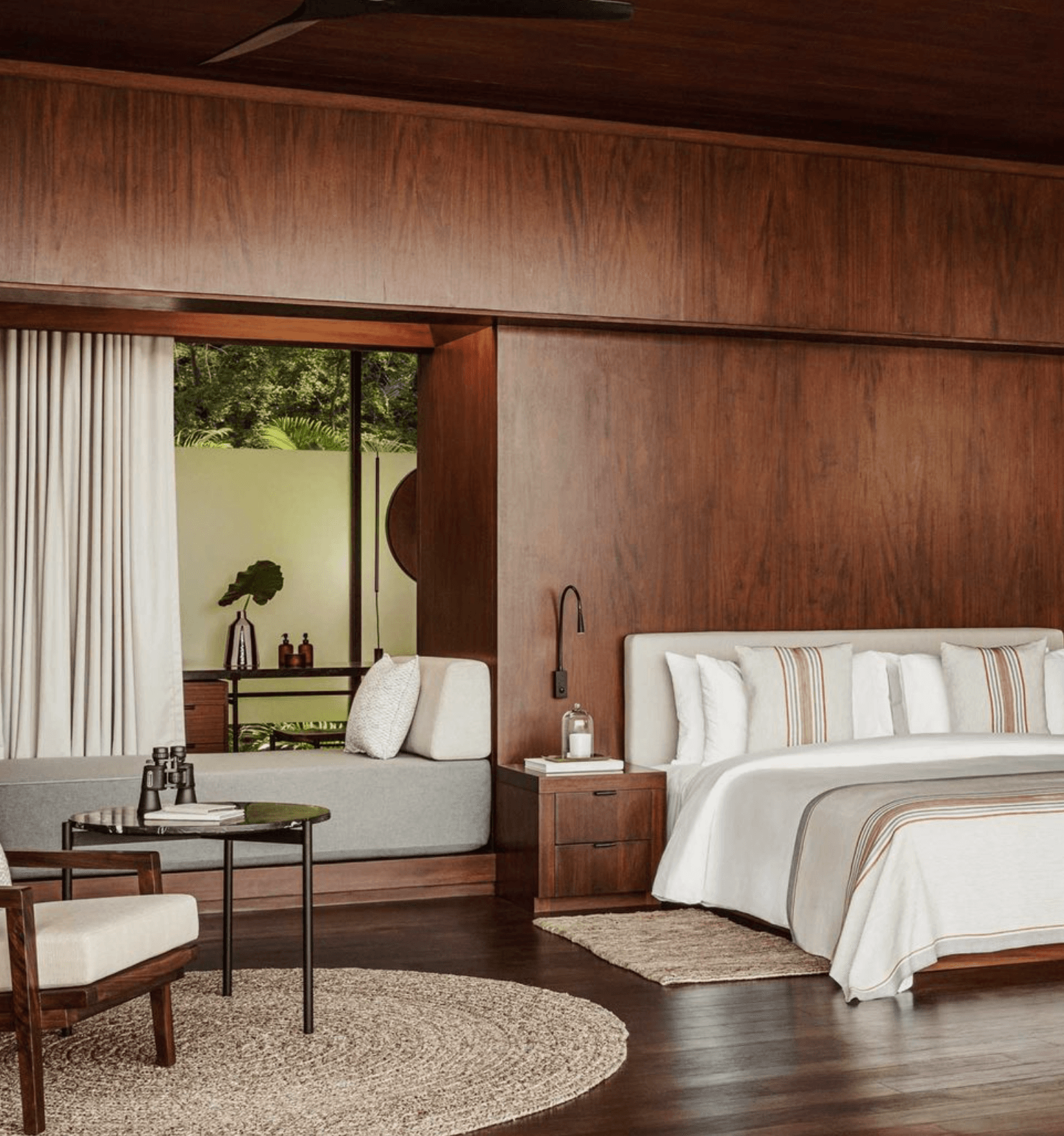 One&Only Mandarina, Mexico — Modernist bedroom with walnut wood paneling, garden-view window seat, neutral linens, and dark hardwood floors.