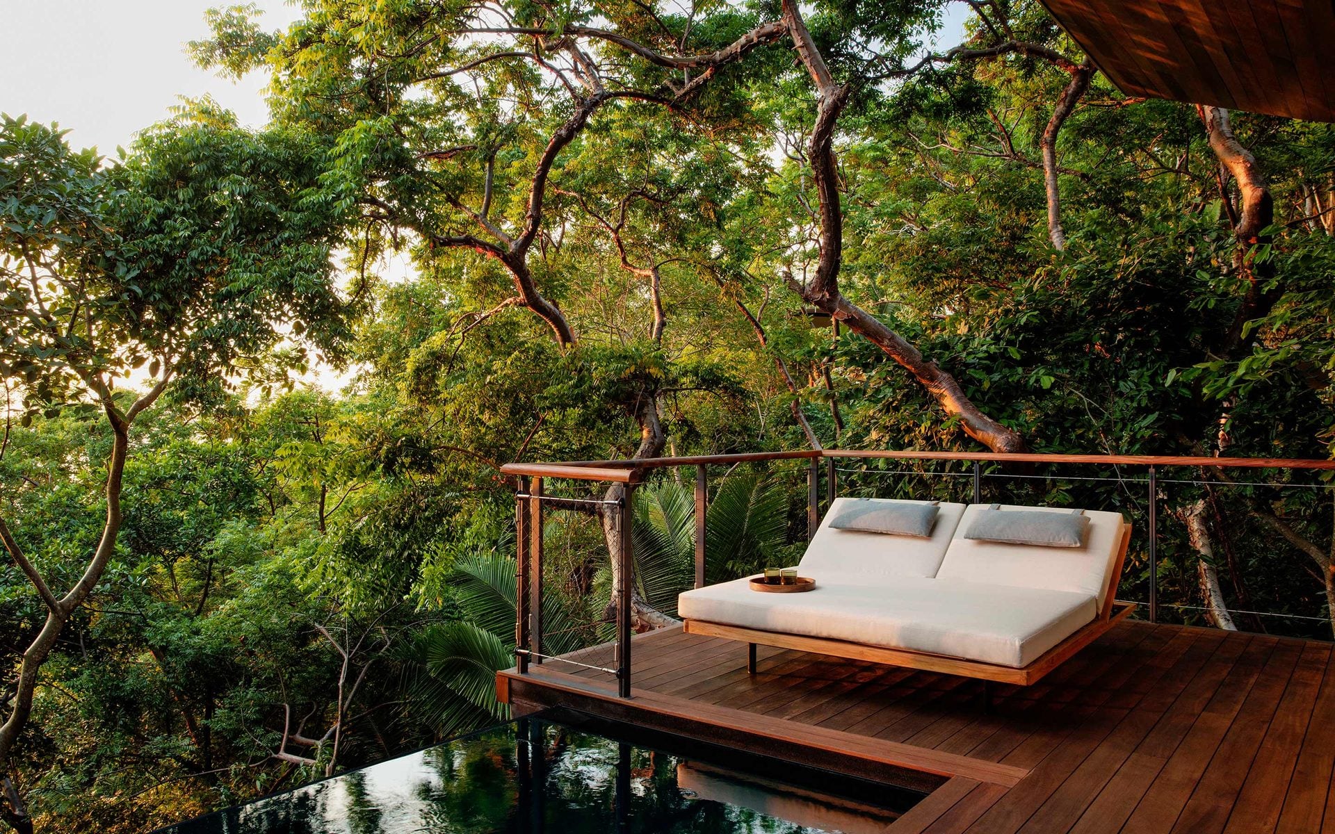 One&Only Mandarina, Mexico — Cantilevered wooden bed deck suspended over forest stream, surrounded by dense jungle canopy and natural light filtering through leaves.