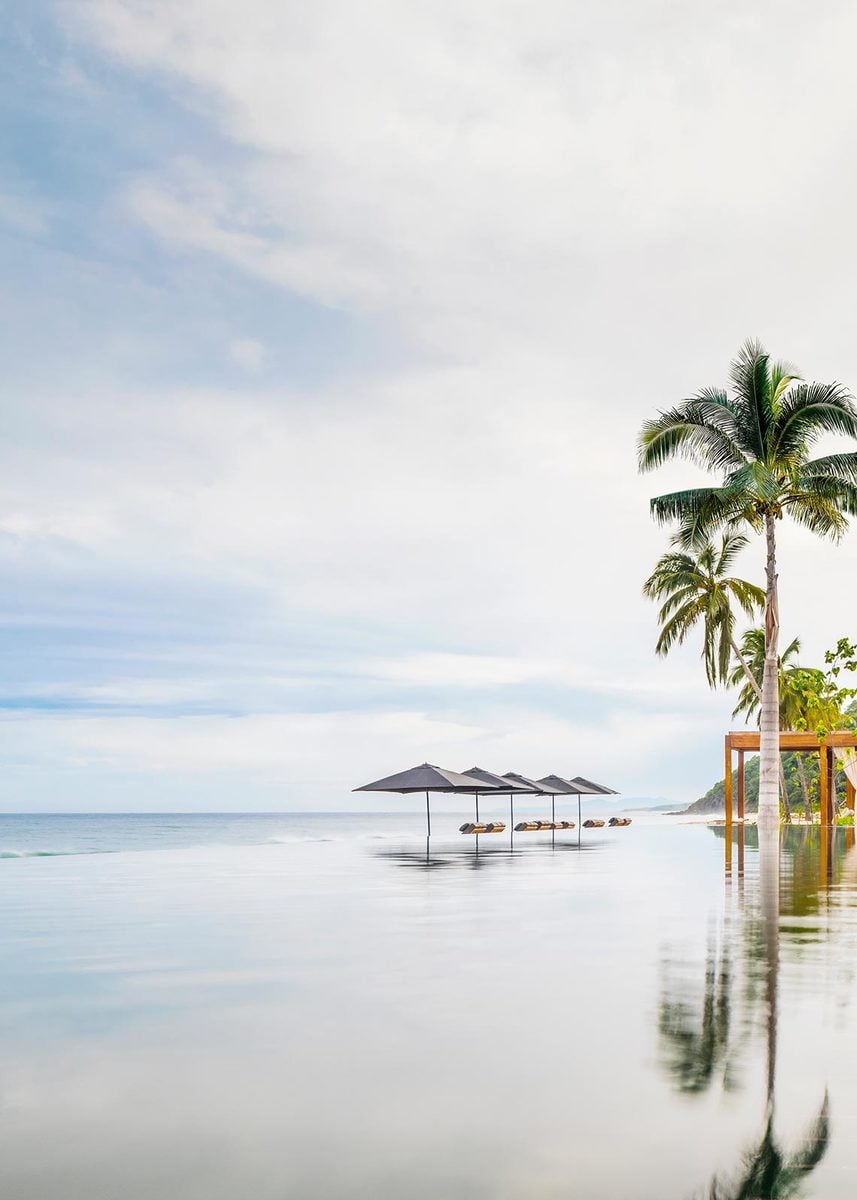 One&Only Mandarina, Mexico — Infinity pool with black umbrellas and palm tree, minimalist architecture reflecting in still water at dawn.