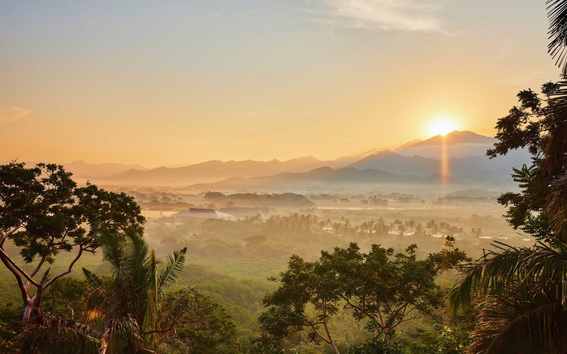 One&Only Mandarina, Mexico — Sunrise over misty valley with volcanic peak, tropical palms and lush forest canopy, warm golden light.