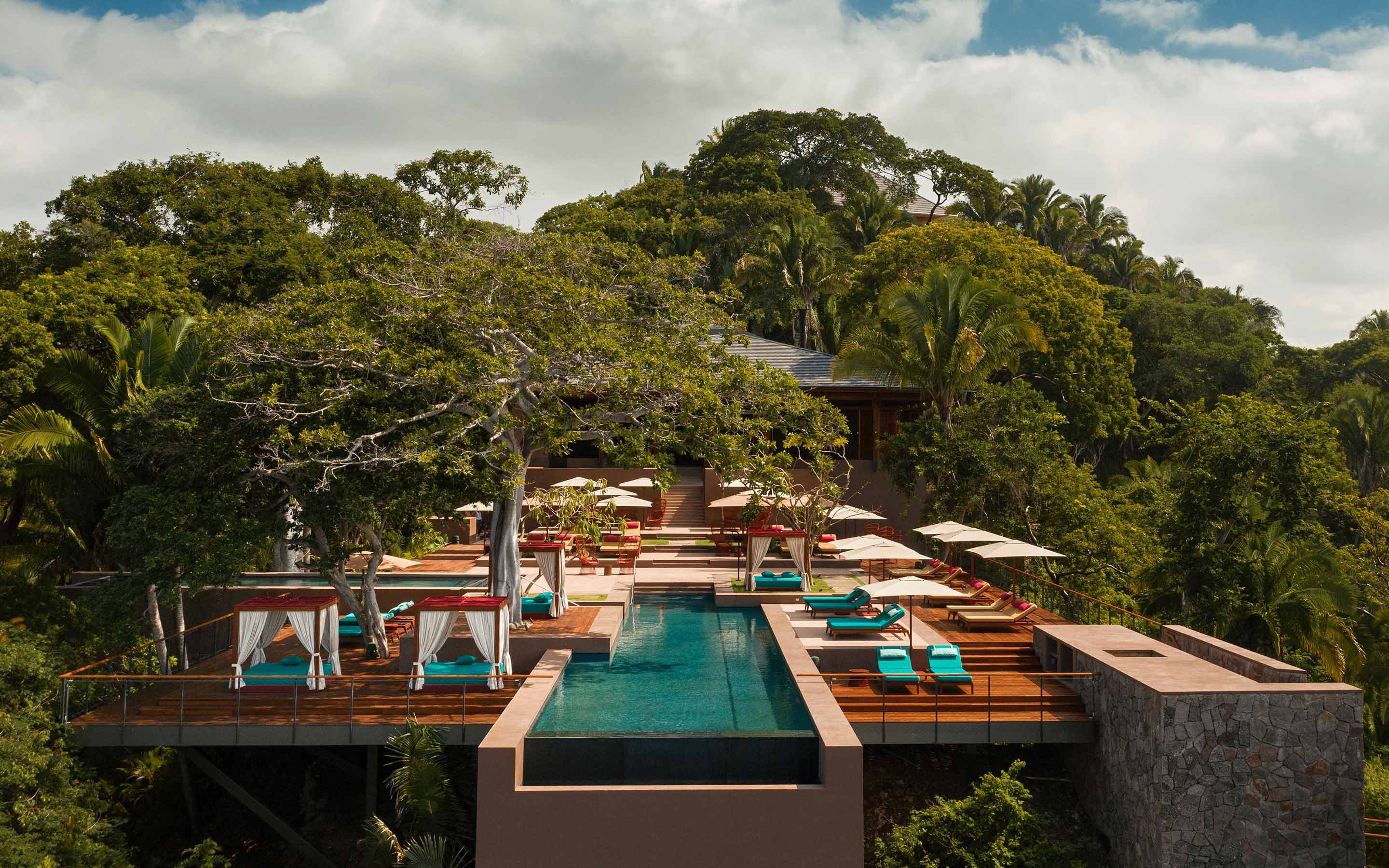One&Only Mandarina, Mexico — Infinity pool overlooking jungle canopy, teak loungers, white cabanas, stone terraces, palm trees, modernist architecture.