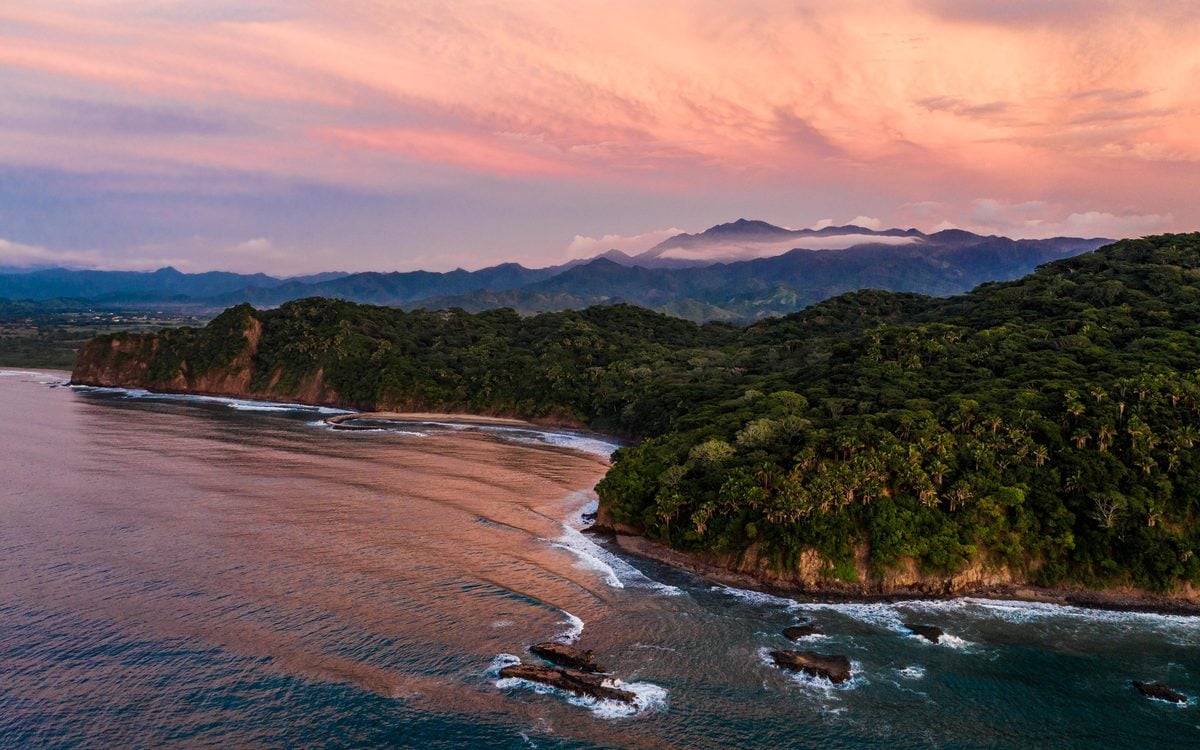 One&Only Mandarina, Mexico — Dramatic Pacific coastline at sunset with lush jungle cliffs, distant mountains, and golden hour light reflecting on water.