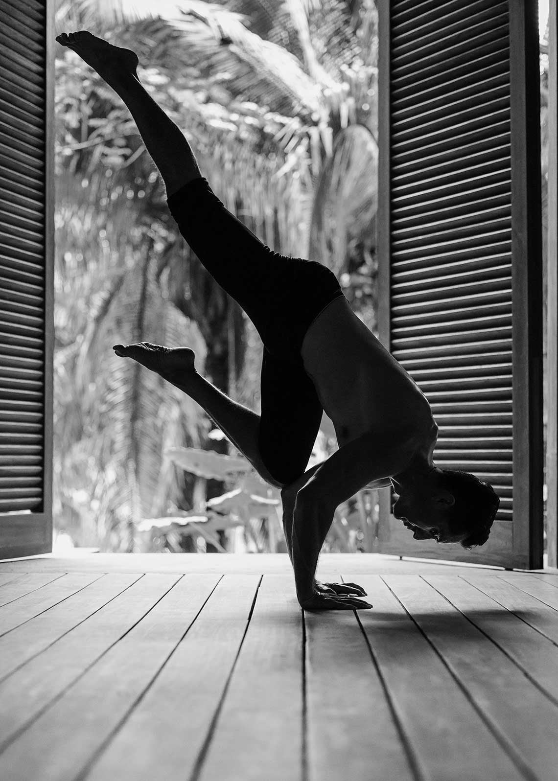 One&Only Mandarina, Mexico — Silhouetted figure in handstand on wooden deck, louver doors and tropical foliage beyond, black and white photography.