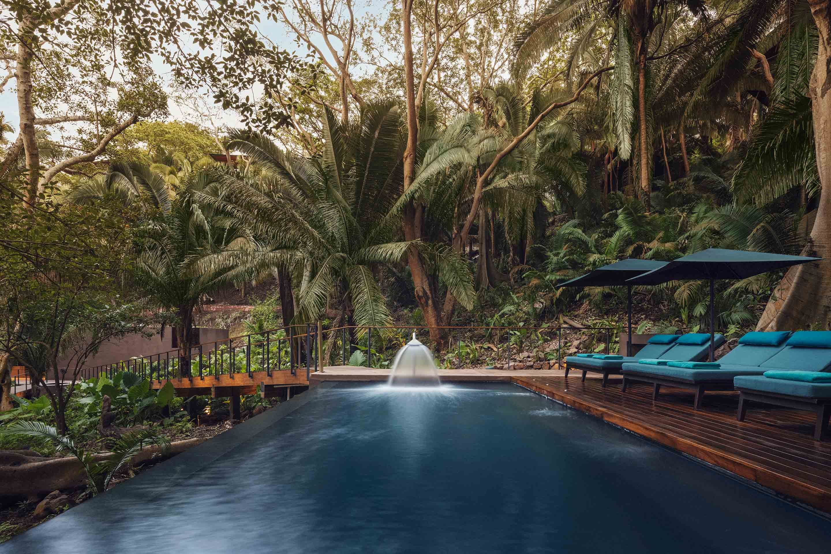 One&Only Mandarina, Mexico — Teak deck with fountain beside sapphire pool, turquoise loungers, palm canopy, morning light filtering through jungle.