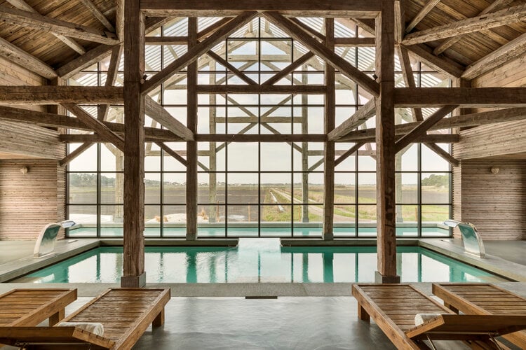 Quinta da Comporta, Portugal — Indoor pool with timber beam architecture, gridded windows framing countryside views, minimalist deck seating, natural light.