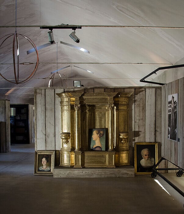 Castello di Reschio, Europe — Gilded Renaissance chapel display with portrait paintings in minimalist gallery space, dramatic spotlighting and concrete walls.