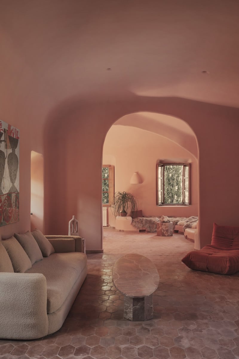 Hotel Corazón, Balearic Islands — Terracotta-pink arched interior with curved sofa, marble table, and warm natural light streaming through windows.