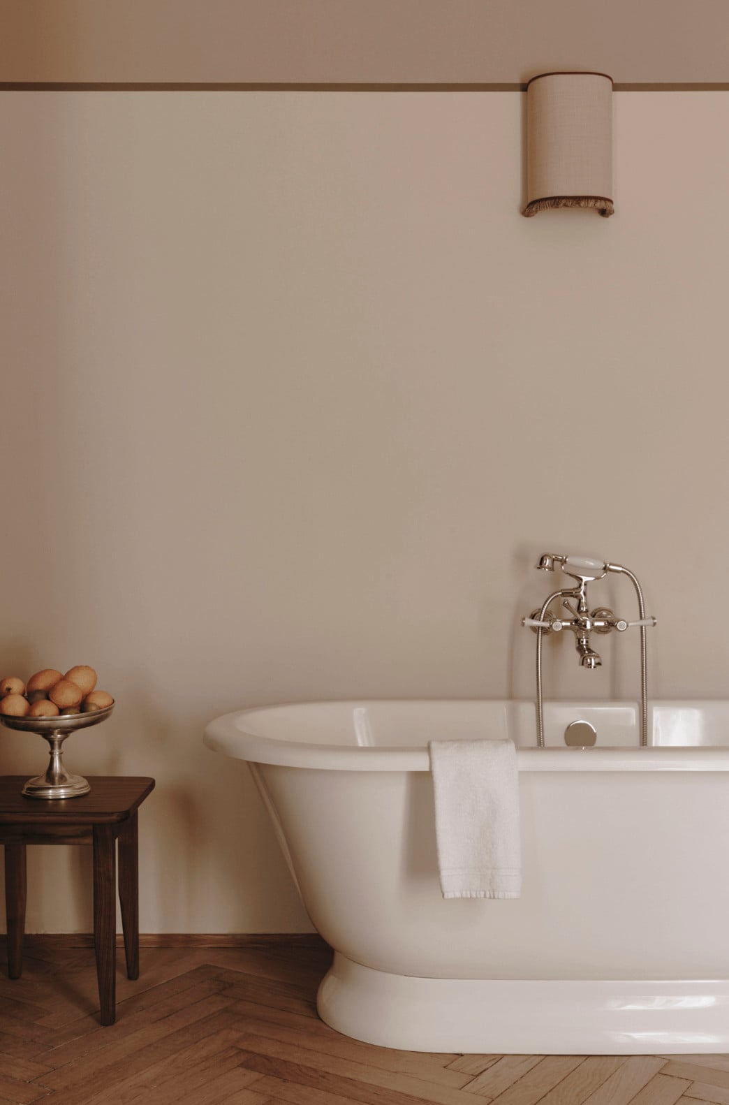 Parkhotel Mondschein, Europe — Minimalist bathroom with freestanding white tub, polished nickel fixtures, cream walls, wooden herringbone floor, and brass bowl of lemons on side table.